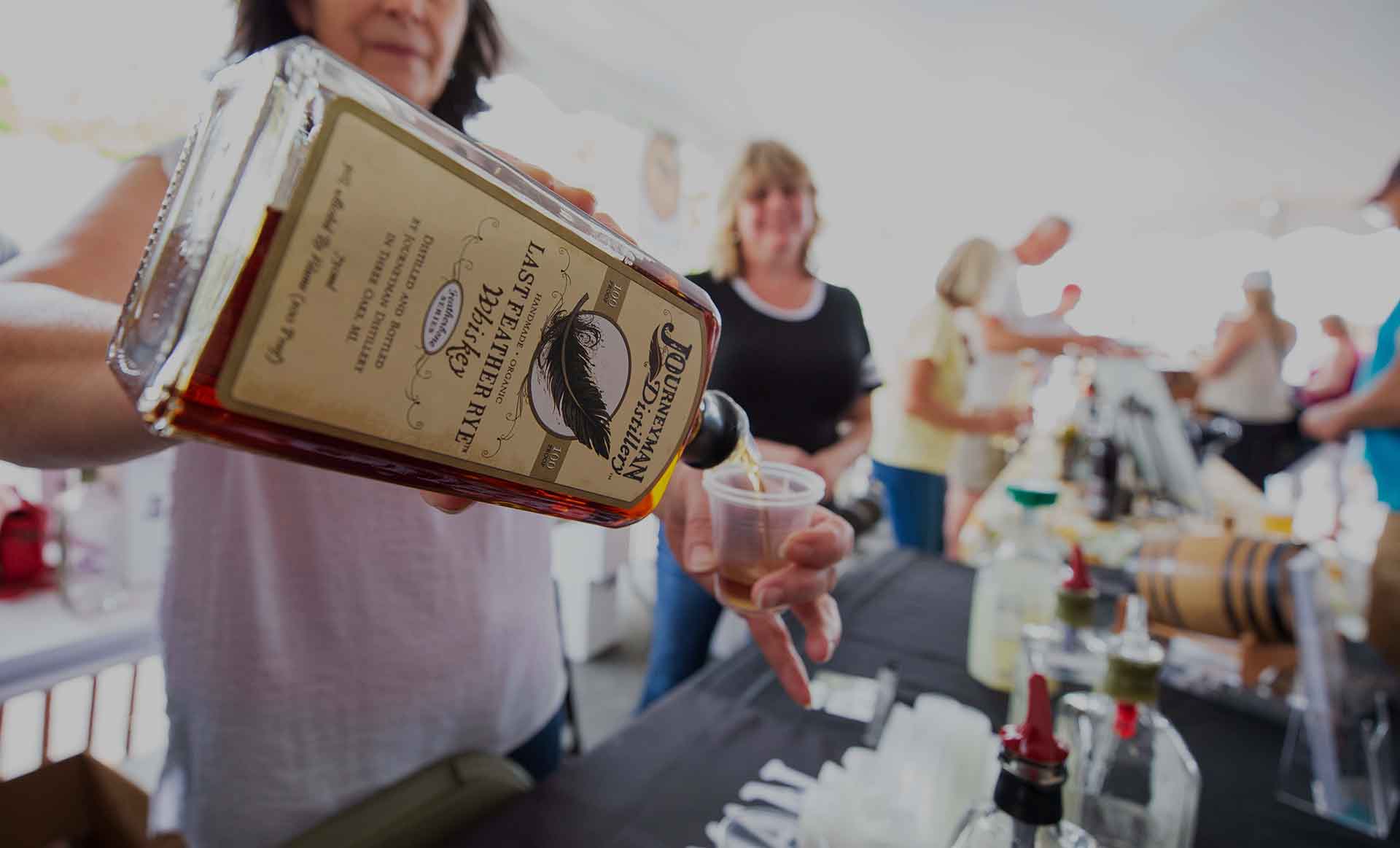 A person pouring a tasting of whiskey at an event.
